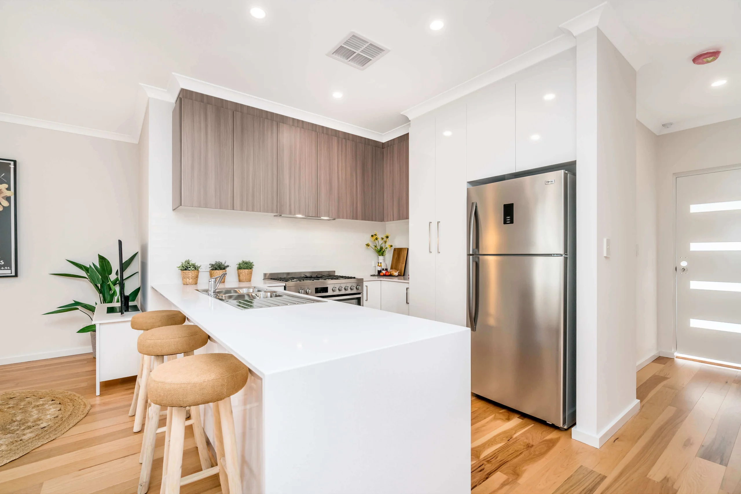 Minimal kitchen with a sculptural white island, pale timber cabinets and curved timber chairs